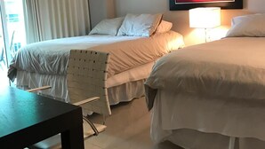 Hotellihuone, jossa on kaksi sänkyä, työpöytä, tuoli, kattotuuletin ja taulu seinällä.