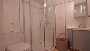 Un baño moderno con ducha de vidrio, inodoro y lavamanos con espejo.