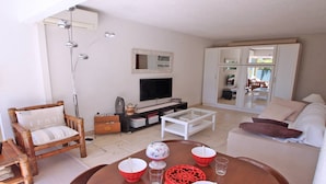 Una sala de estar con sofá, sillón, mesa de centro, televisor y una zona de comedor con mesa y sillas.