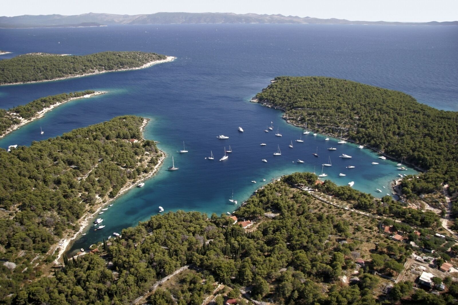 An aerial view of a coastal area with clear turquoise waters, surrounded by dense green forests and small islands.