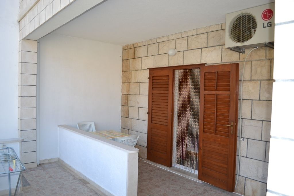 A small balcony with a white railing, a wooden door with a decorative curtain, and an air conditioning unit mounted on the wall.