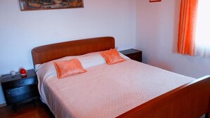 A neatly made bed with a wooden headboard and two pillows, a nightstand with a red object on it, and a painting on the wall. - Apartment in Poljana with Seaview, Balcony, Air condition, WIFI (4232-3) (Poljana)