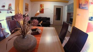 Un espace repas comprenant une longue table en bois, des chaises et un vase contenant des plantes séchées.