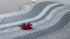 Un lit bien fait, recouvert d’une couverture à rayures et agrémenté d’une seule fleur rouge.