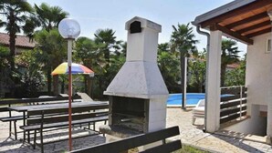 An outdoor patio area with a stone-tiled floor, a barbecue grill, and a pool in the background. - Apartment in Poreč with Terrace, WIFI (819-3) (Porec)