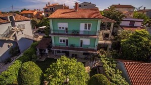 A two-story building with a red-tiled roof, a balcony on the second floor, and a small garden area with trimmed bushes.
