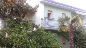 A two-story building with a balcony, surrounded by dense greenery and a palm tree.