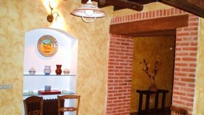Comedor con paredes de ladrillo, una mesa de madera y sillas. Se observa una estantería con objetos decorativos y una lámpara colgante.