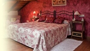 Un dormitorio con una cama grande, techo de madera, pared roja y un cuadro enmarcado sobre la cama.