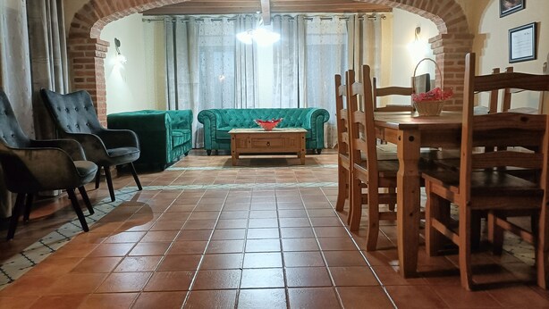 Una sala de estar con un sofá verde, dos sillones, una mesa de centro de madera y una zona de comedor con una mesa y sillas de madera.