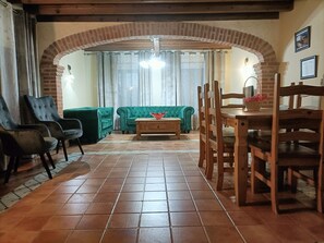 Una sala de estar con un sofá verde, dos sillones, una mesa de centro de madera y una zona de comedor con una mesa y sillas de madera.