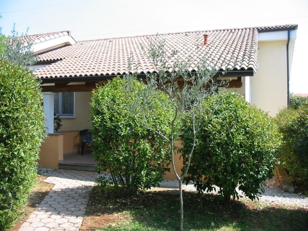 Une maison avec un toit en tuiles, un chemin de pierre menant à l’entrée et un petit jardin agrémenté d’arbustes.