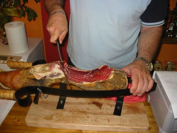 A person carving a large piece of meat on a wooden cutting board.