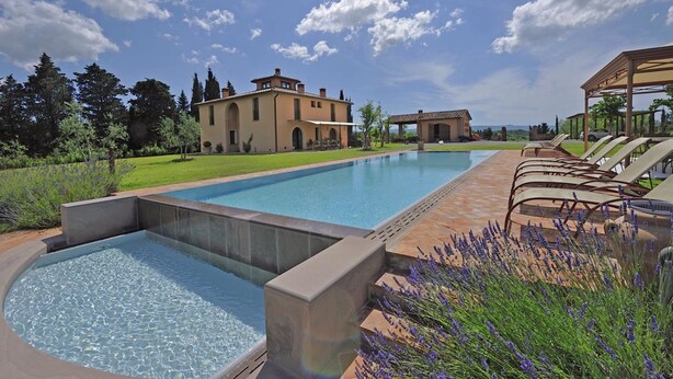 A swimming pool with a patio area, a large house with arched windows, and a clear sky. - Villa for 11 People in Tuscany with private pool (Peccioli)