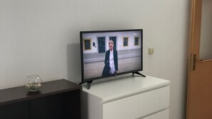 Ein Fernseher steht auf einer weißen Kommode in einem Zimmer mit Fliesenboden und einer Holztür.