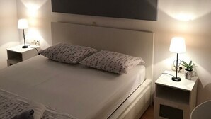 Ein modernes Schlafzimmer mit einem großen Bett, zwei Nachttischen mit Lampen, einer Wandklimaanlage und einer Leuchtstreifen-Deckenlampe.
