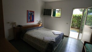 Ein Schlafzimmer mit Bett, Nachttisch, Lampe, einem Gemälde, einem Fenster und einer Glastür zum Balkon.