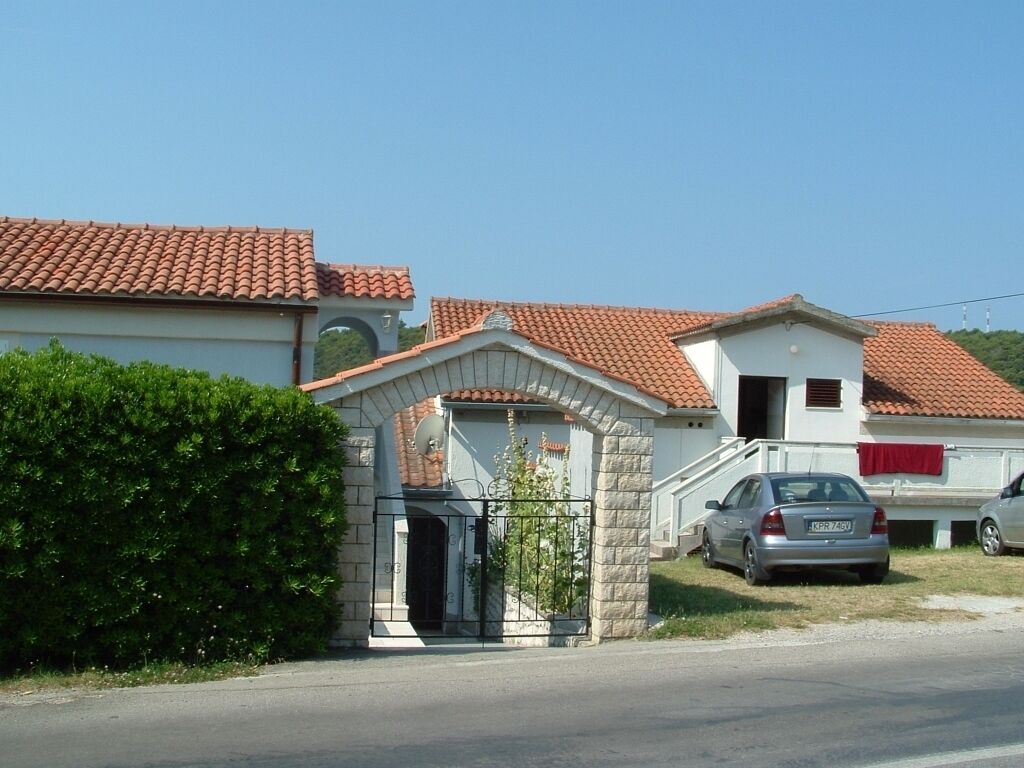Un quartier résidentiel avec une maison dotée d’un toit en tuiles, d’une entrée en arc de pierre et d’une voiture garée dans l’allée.