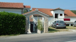 Un quartier résidentiel avec une maison dotée d’un toit en tuiles, d’une entrée en arc de pierre et d’une voiture garée dans l’allée.