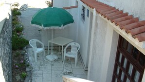 Une petite terrasse extérieure avec une table et deux chaises, un parasol vert et un mur en pierre.