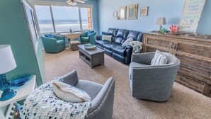 Una sala de estar con vista al océano, un sofá azul, un sillón gris y un aparador de madera.
