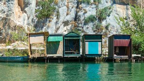 A row of floating houses with wooden structures and open sides, situated on calm water with a rocky cliff in the background. - Apartment in Duće with Air condition, WIFI, Washing machine (4166-1) (Duce)