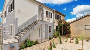 A two-story house with a staircase, a small balcony, and a garden with various plants and flowers.