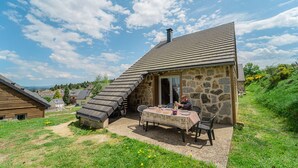 A stone building with a sloped roof, a table with chairs, and a person seated at the table.