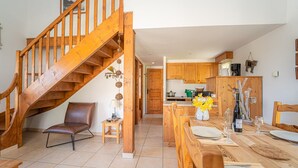 A spacious kitchen with wooden cabinets, a dining area with a table set for two, and a wooden staircase leading to an upper level.