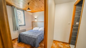 Ein Schlafzimmer mit Bett, einem fensterbelaubten Fenster, einer Holzbalkendecke und einem gefliesten Boden.