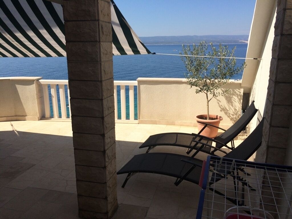 A balcony with two lounge chairs, a potted plant, and a view of the sea.