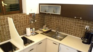 A compact kitchen with white cabinets, a built-in microwave, a sink, and a coffee maker.