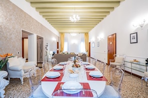 A dining room with a long table set for a meal, clear chairs, and a chandelier.