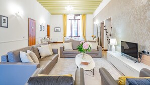 A modern living room with a sofa set, a coffee table with a vase, a flat-screen TV, and a dining area with chairs and a table. - Ca' Del Monastero 4 Collection (Venezia)