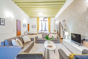 A modern living room with a sofa set, a coffee table with a vase, a flat-screen TV, and a dining area with chairs and a table. - Ca' Del Monastero 4 Collection (Venezia)