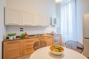 A modern kitchen with wooden cabinets, a stainless steel sink, and a bowl of fruit on the table.