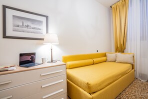 A room with a bed, a desk with a laptop, a lamp, and a framed picture on the wall.