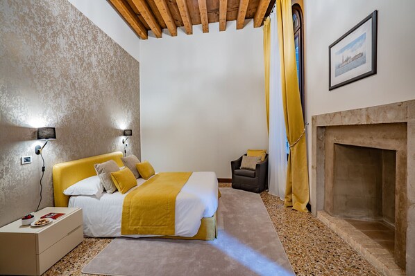 A bedroom with a bed, bedside table, lamp, chair, and a fireplace.
