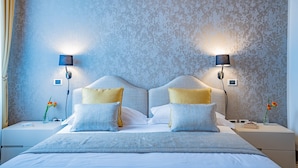 A neatly made bed with two pillows, a bedside table with a lamp, and a wall with a textured pattern. - Ca' Del Monastero 4 Collection (Venezia)