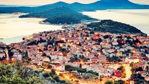 A coastal town with a central church, surrounded by residential buildings and a mountainous backdrop. - Apartment in Mali Lošinj with Terrace, Air condition, Washing machine (3683-1) (Mali Lošinj)