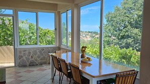 Un comedor con una mesa grande y sillas, ventanas amplias con vistas a zonas verdes y edificios, además de una pared de piedra.