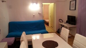 A small, well-lit room with a blue sofa, a white table with a chocolate cake, and a TV on a desk. - Apartment in Zagreb with Balcony, WIFI, Washing machine (4292-1) (Zagreb)