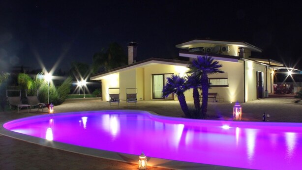 A modern house with a swimming pool at night, illuminated by purple lights.