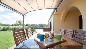 An outdoor patio with a glass table, wooden chairs, and a variety of colorful cups and bowls.