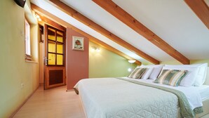 A bedroom with a large bed, wooden beams, a window, and a door.