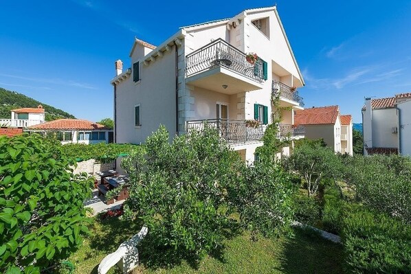 A two-story building with a balcony, surrounded by greenery and other buildings. - Apartment in Bol with Balcony, Air condition, WIFI, Dishwasher (5217-7) (Bol)
