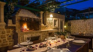 An outdoor dining area with a stone fireplace, a table set for two with wine glasses and plates, and a pergola overhead. - Apartment in Bol with Balcony, Air condition, WIFI, Dishwasher (5217-7) (Bol)