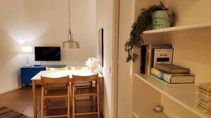 Un coin repas avec une table et des chaises, un téléviseur, une lampe et une bibliothèque contenant des livres et une plante.