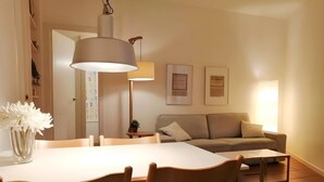Un coin repas comprenant une table, des chaises, une lampe suspendue, un canapé et des certificats encadrés accrochés au mur.