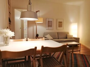 A dining area with a table, chairs, a hanging lamp, a sofa, and framed certificates on the wall.